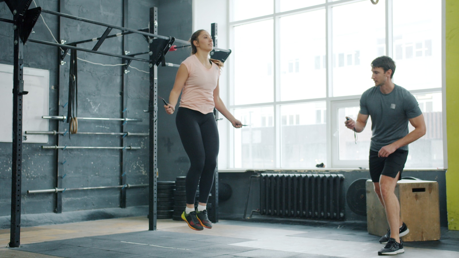 Woman jumps rope while man watches in gym.
